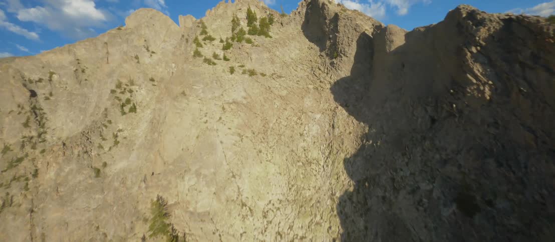 Traveling over jagged rocky mountain ridges dotted with green trees and patches of snow on a bright blue sky day