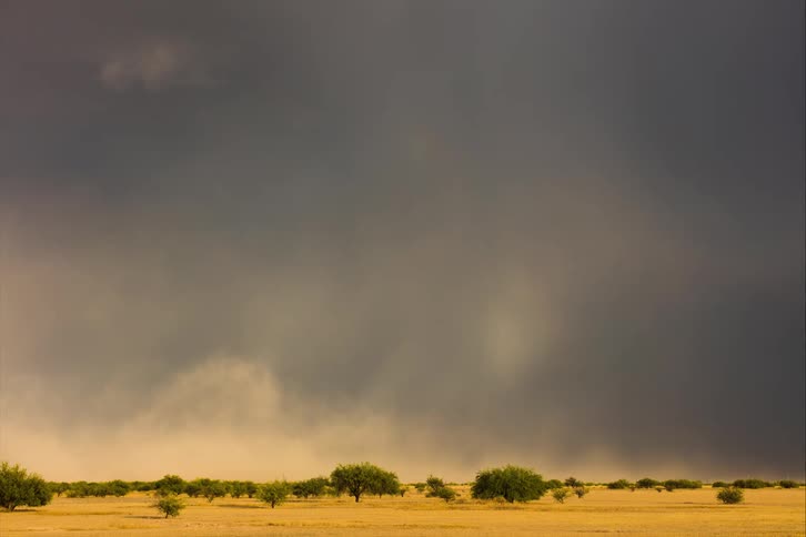 A rainbow hangs over a vast plain before clouds sweep through the sky and engulf it
