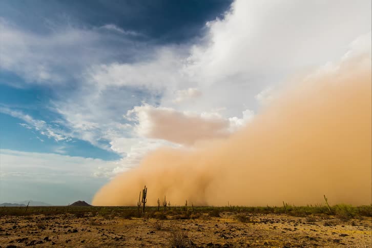 A slow moving thick dust cloud turns the sky dark over a barren desert