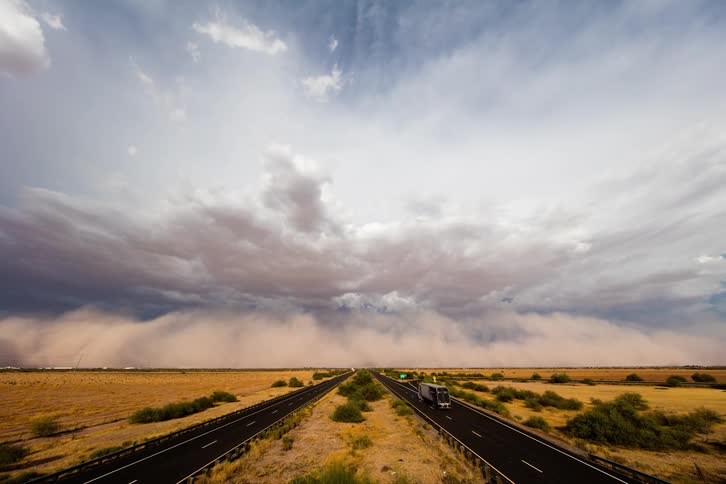 Two roads with vehicles in a desert with the sky and clouds in the background