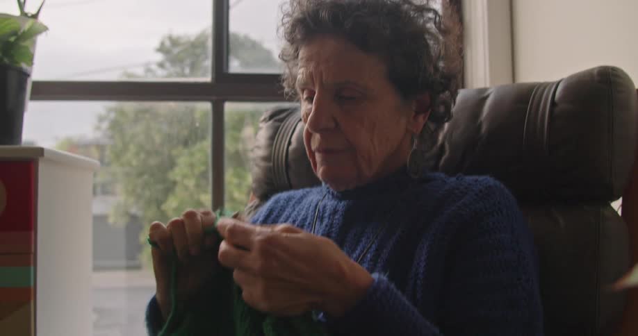 An elderly woman knitting while sitting in a living room chair