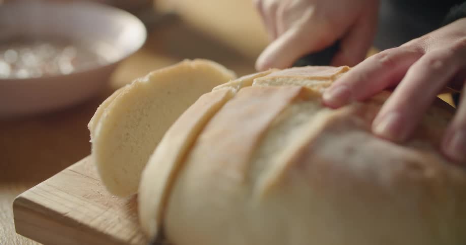 Person slices oval bread loaf on wooden chopping board