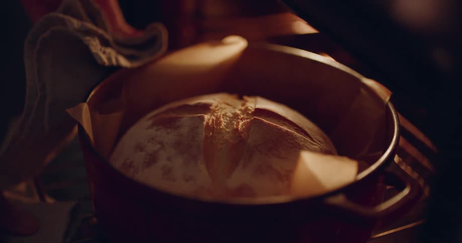 A person carefully pulls a loaf of bread from the oven and touches it to check if it is ready