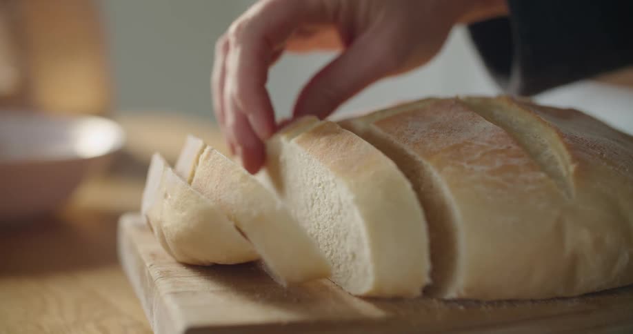 A hand reaches for and picks up a slice of freshly baked bread