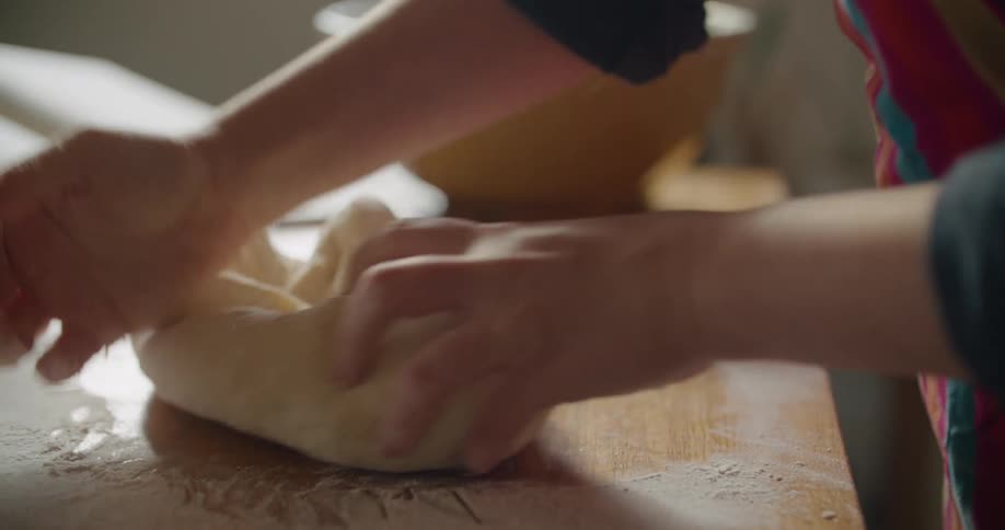 Baker kneads dough on wooden topped counter