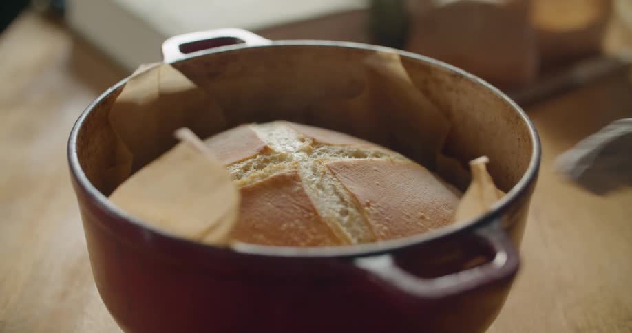 Hands place a hot pot with freshly baked bread on a wooden kitchen counter