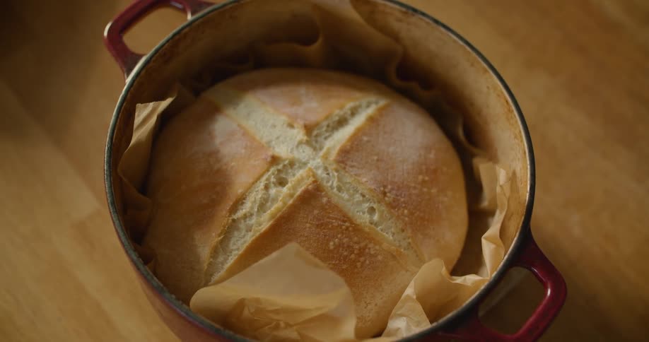 A person with a towel placing a pot with a baked good on a piece of wood on a table