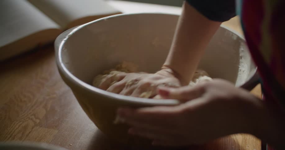 A person in a room kneading dough in a bowl on a table