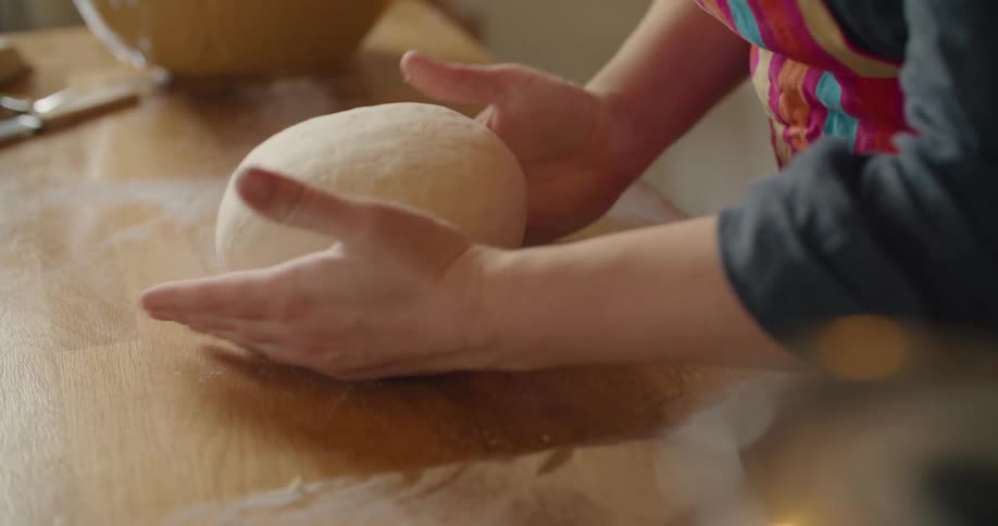 Woman rotates ball of dough on wooden surface