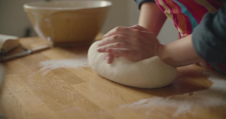 A person kneads dough with their hands on a wooden kitchen counter