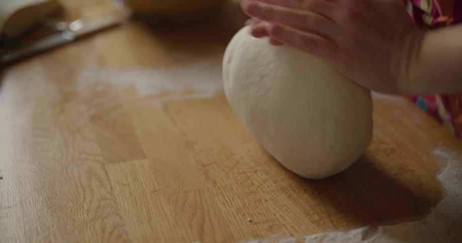 Hands knead and roll dough on a floured wooden kitchen counter