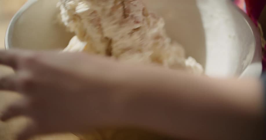 Baker mixes dough in white bowl with hands