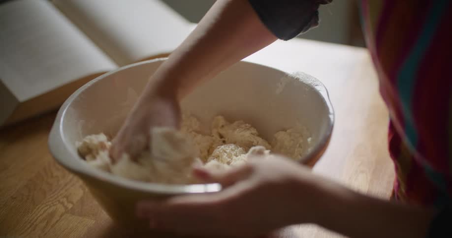 A person uses their hand to mix a soft dough in a large bowl