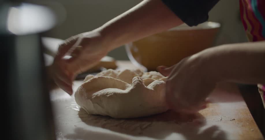 Person kneads dough on wooden counter top near bowl and open cookbook