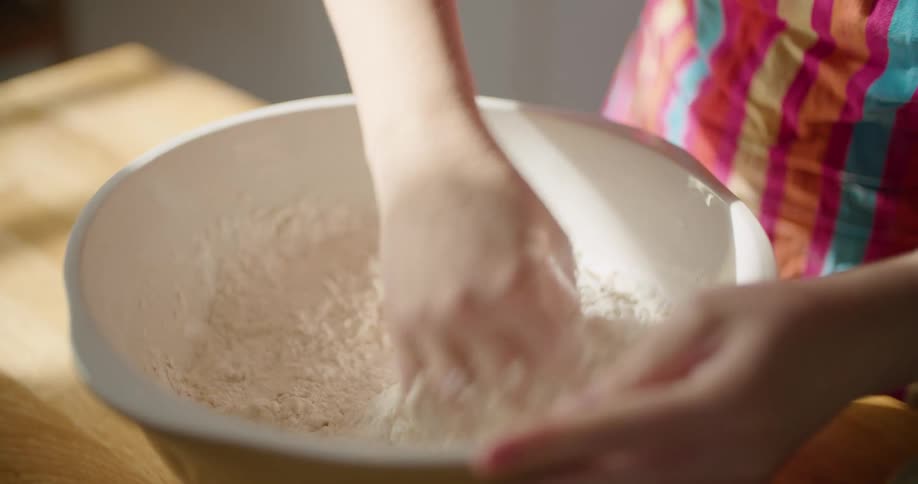 Woman mixes contents from one bowl into soft dough in another bowl using her hand