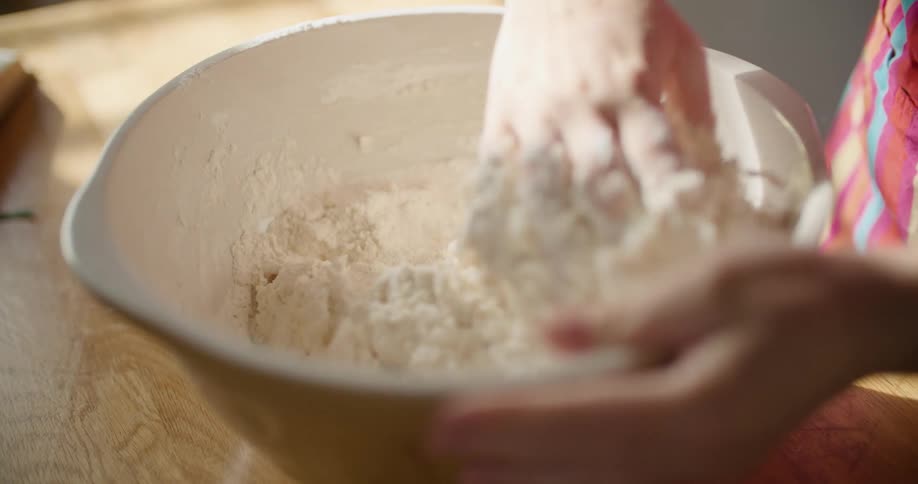 A woman uses her bare hand to mix flour and other ingredients in a large bowl