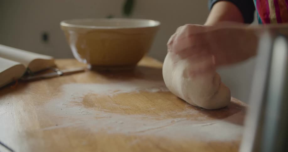 A person in a room kneading dough on a table with flour