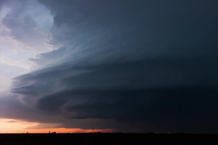 Dark gray storm clouds rotate and flow over town and red colored horizon