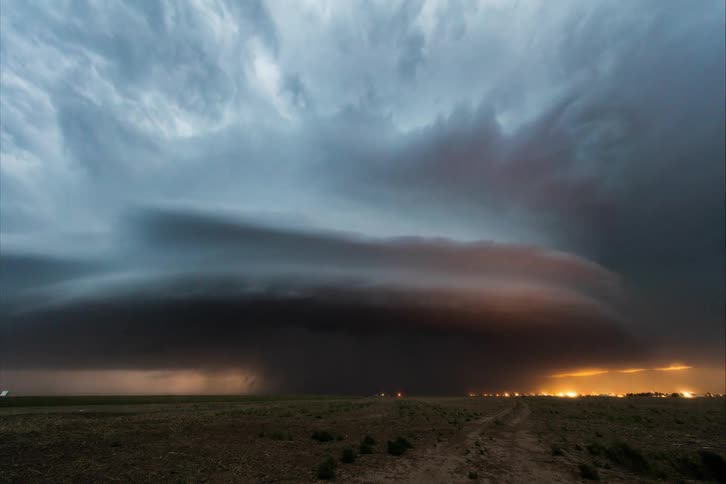 Storm clouds are in rotation as a tornado moves above the ground and lightning is flashing