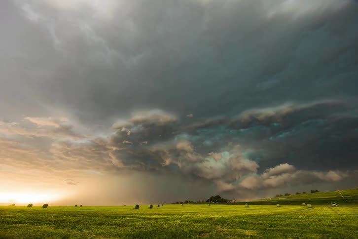 Gray storm clouds flow across fields dotted with hay bales as traffic moves along road