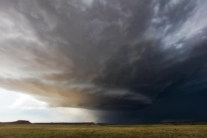 Storm clouds flow across plains and nearby mesa as vehicles moves down road