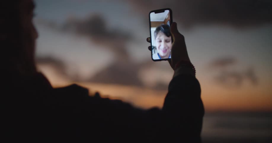 Man standing on the beach laughs talking to his son on a video call at sunset