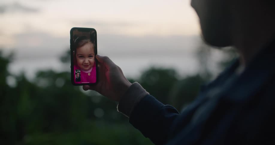 A person holds their cell phone having a video call outside with a toddler girl