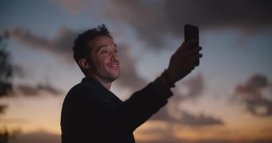 A man holds a cell phone up having a video call outside with the night sky in the background