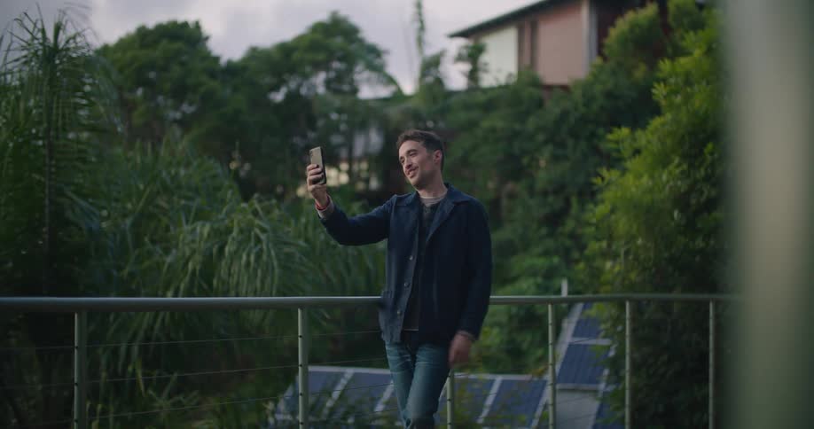A man smiling and blowing kisses at a smartphone while video chatting outside