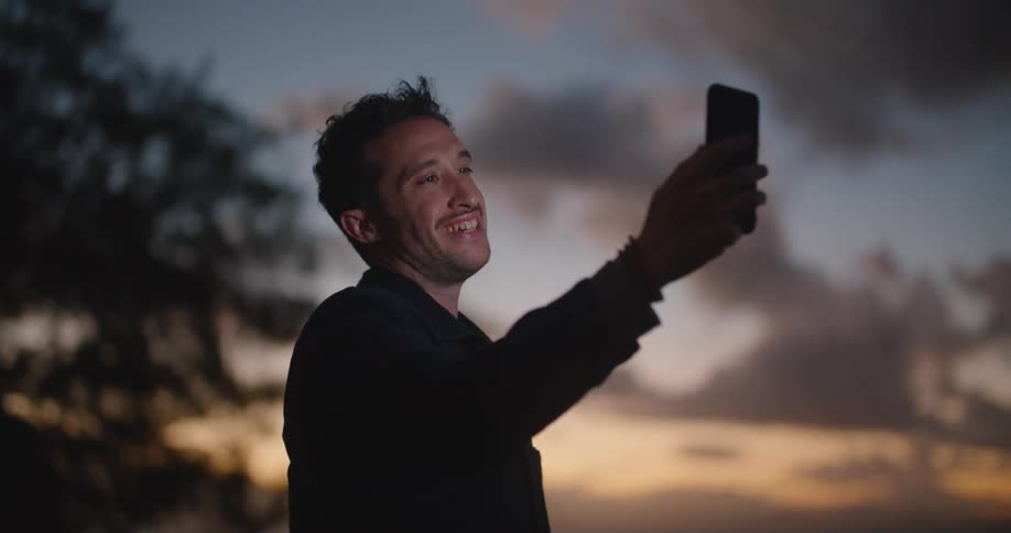 Young man talking on a video call on a smartphone in the beach at sunset