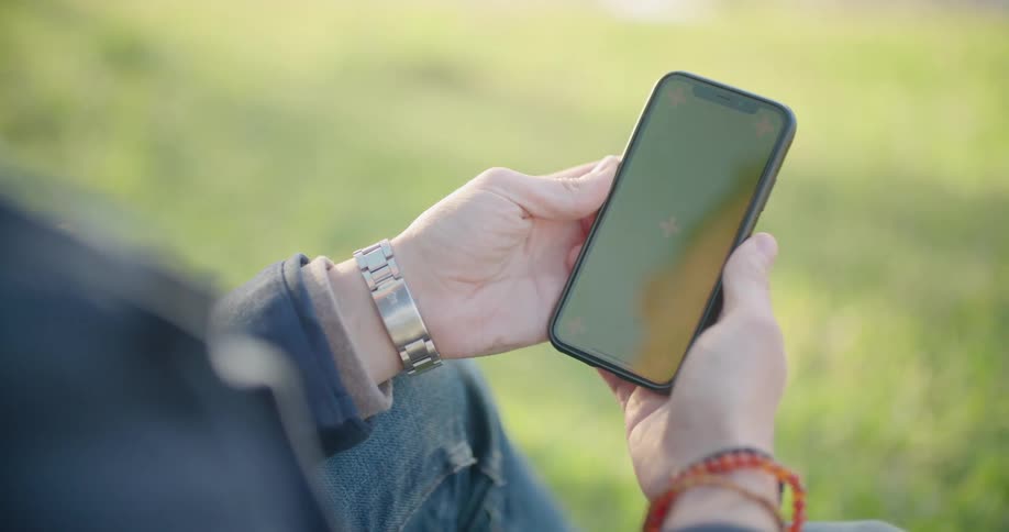 A person sitting on the green grass holding a smartphone