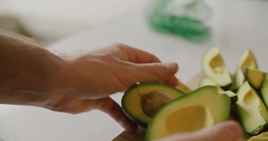 A man twists open a cut avocado and places it on a cutting board filled with avocado wedges