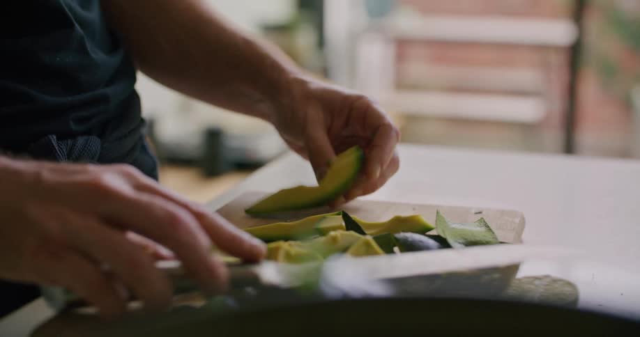Mans hands cut an avocado with a knife on the cutting board in the kitchen
