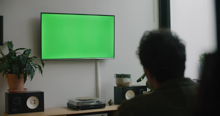 A man sits at home and yells as he looks at a green television screen