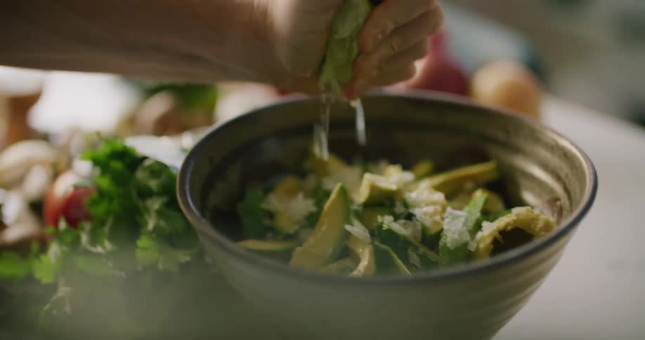 A person squeezes lime juice over a bowl of avocado