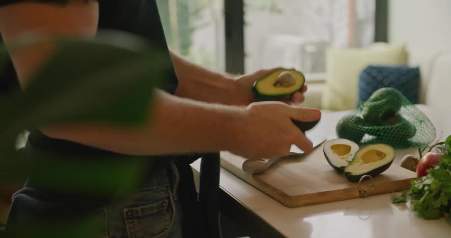 A person in a room cutting avocados with a knife over a cutting board