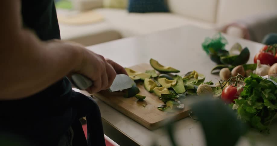 A person in a room cutting avocados with a knife on a cutting board