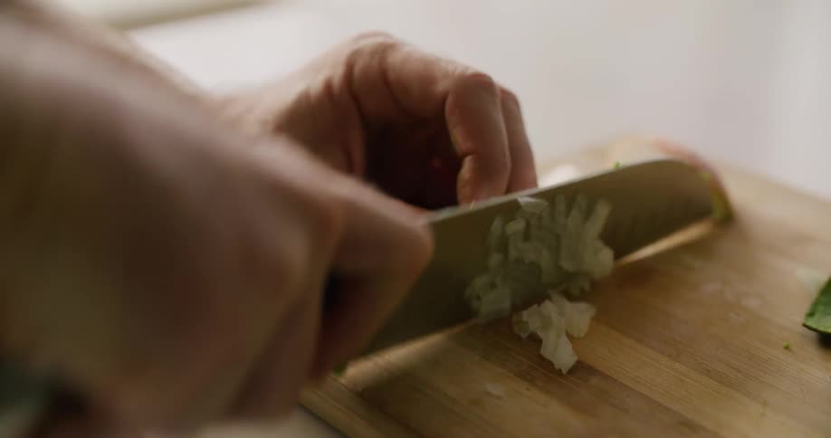 A person uses a knife to chop a vegetable in small pieces