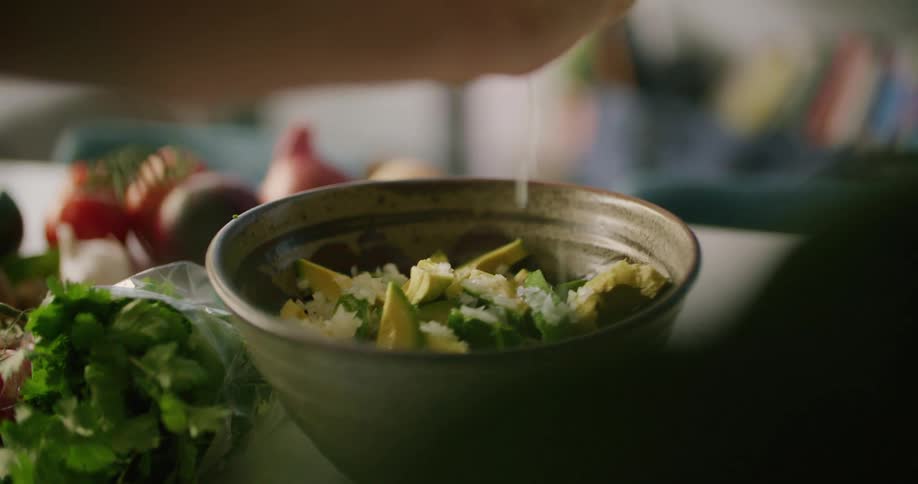 A person squeezes lime juice over a bowl of avocado