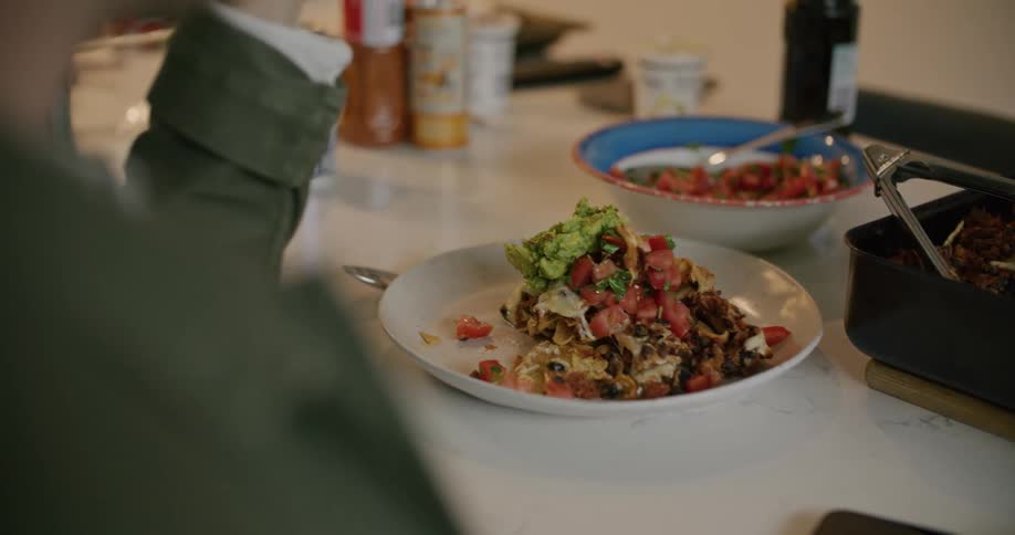 A man sitting at a table in a room as another person places food on his plate with a wall in the background