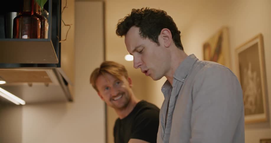 Men cook together and talk in kitchen smiling as one tastes food