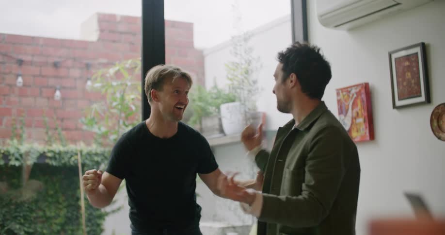 Two men jump off of the couch excited and high five each other