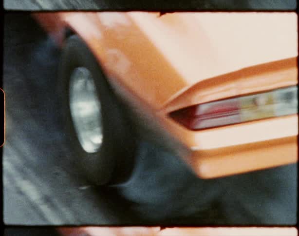 An orange muscle car spins its wheels as the driver accelerates extremely quickly