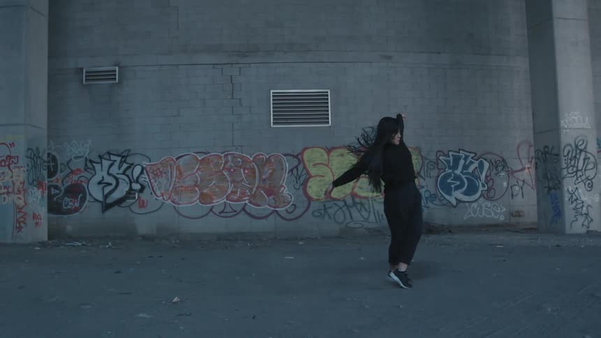 Young woman dancing in front of a gray brick wall covered in graffiti