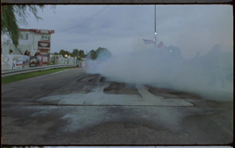 Car races down road kicking up smoke as it burns rubber