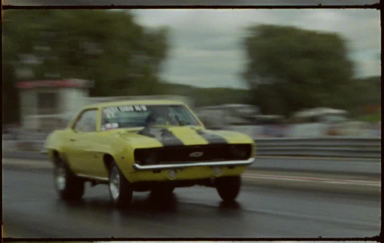 A pair of cars compete in a drag race on a race track on a cloudy day