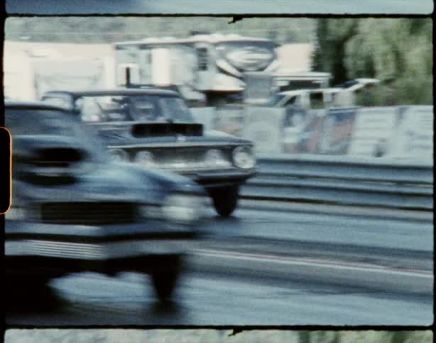 Car with racing engine speeds down track as people walk around near