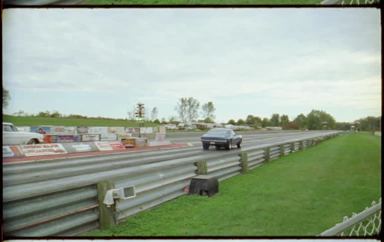 Film footage of people watch as two cars race on a track