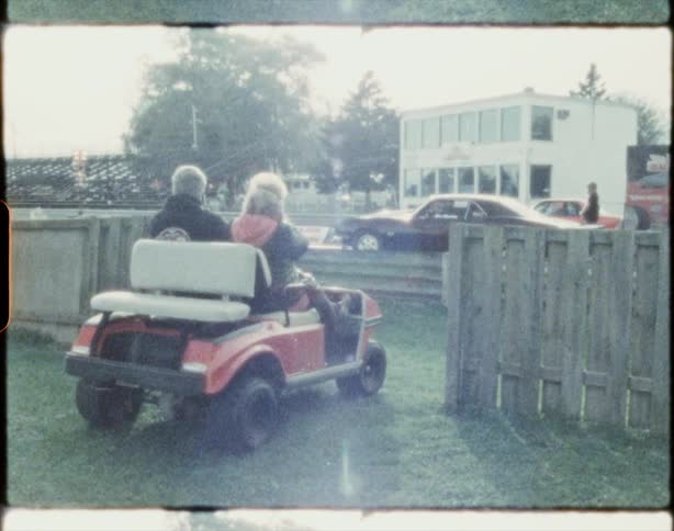 Couple sits in small cart watching race cars start during race