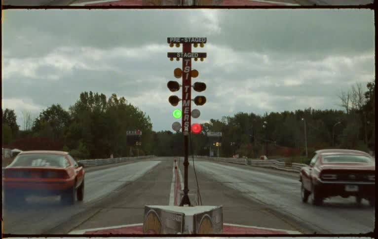 Two cars race down the road on the green light